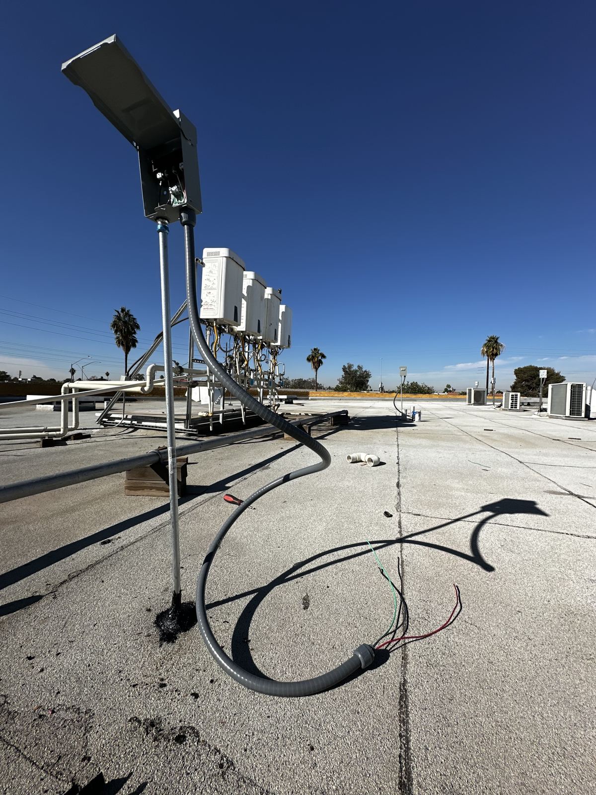 Pole light and conduit run at a commercial property, with the parking area behind.