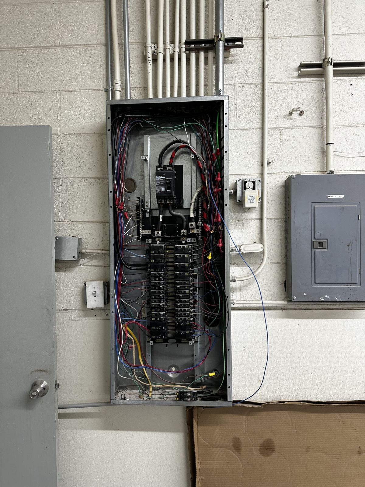Exterior electrical service equipment and conduit runs mounted on a block wall.